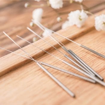 Photo of acupuncture needles on a wooden surface with flowers in the background.