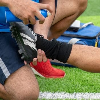 A foot in a cleat being sprayed with a medication for an injury while playing soccer.