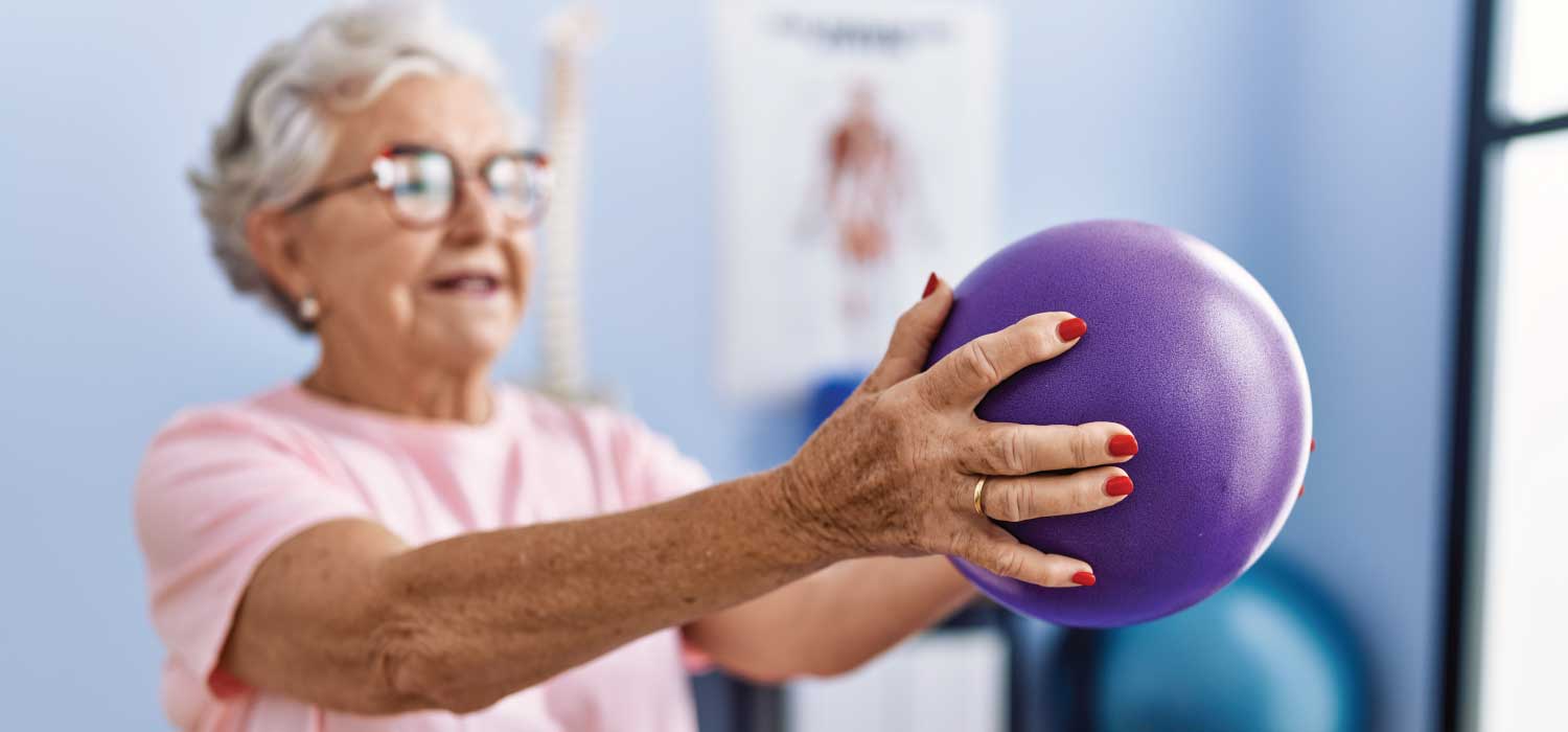 Senior lady holding a purple ball doing physical therapy