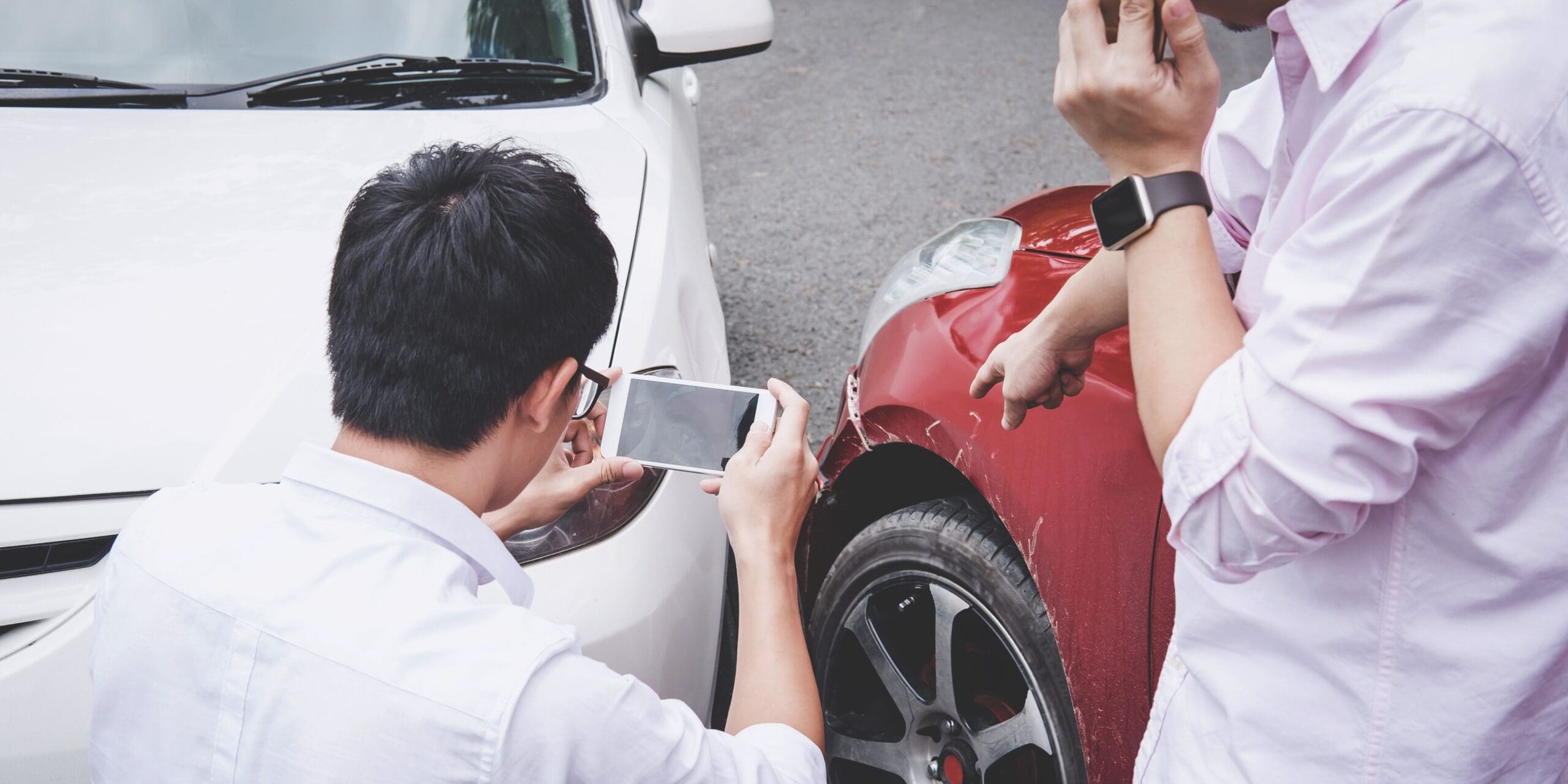 The back of a person's neck taking a photo of damage to a vehicle after an accident