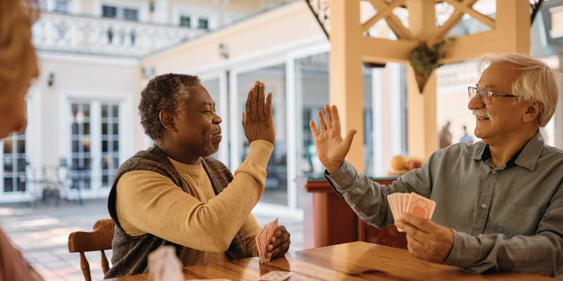 Two seniors high-fiving each other while playing cards.