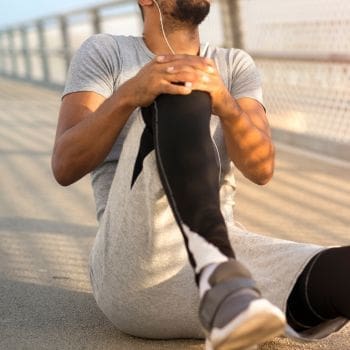A runner sitting on the ground of a bridge, holding his right knee as if it is injured.