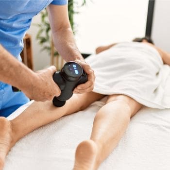 A female laying on a therapy table with a therapist using a massage tool on the back of her left leg.