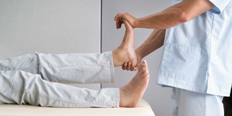 A medical provider flexes and stretches a patient's left foot while they lay on an exam table.