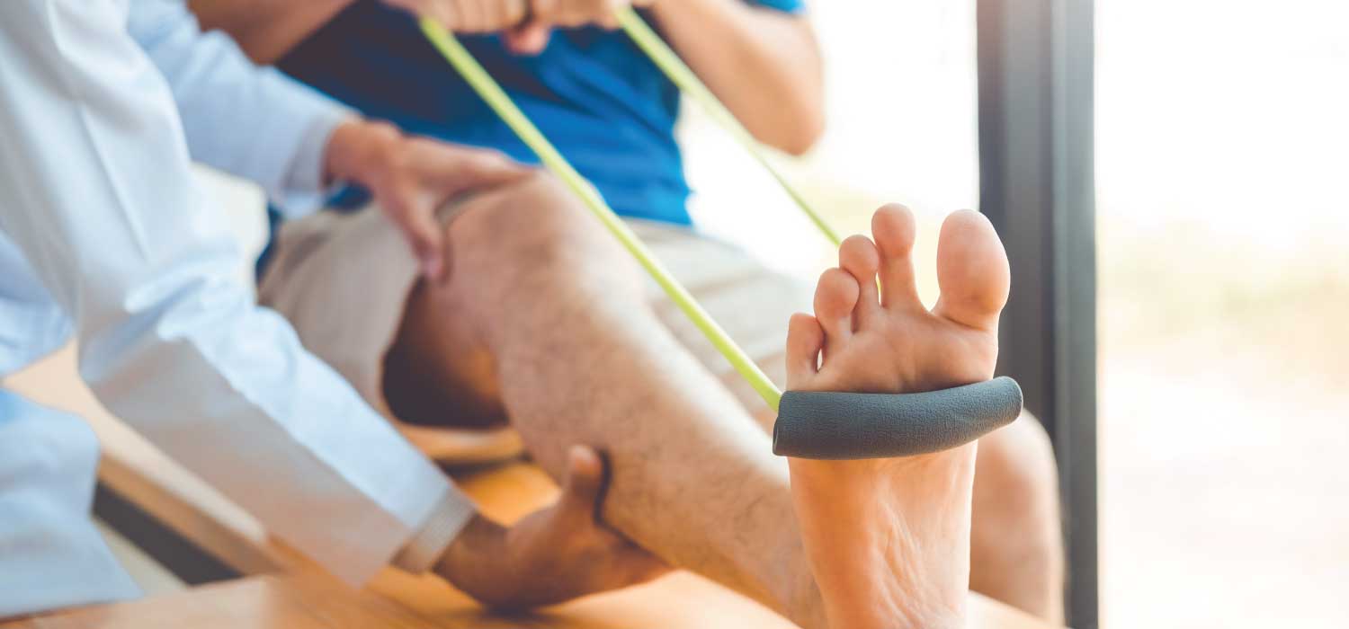 A patient has their leg extended with a resistance band held by their foot while assisted by a medical provider for physical therapy.