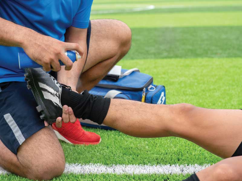 Image of a soccer player's left ankle being help by a therapist and treated on the field for an injury.