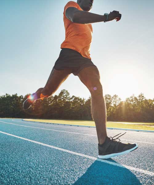 A male wearing an orange shirt and black shorts running on a track.