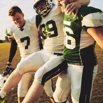 An injured football player being supported by two other football players off the field.