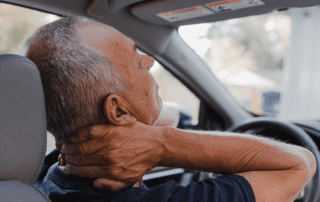 A male driver sits in the driver seat and holds his neck in pain.
