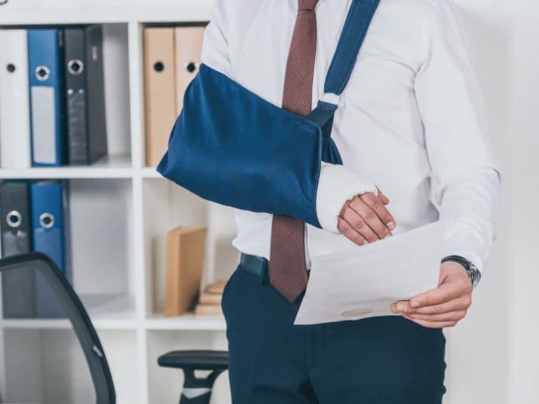 A man in business professional has his right arm in an arm sling and holds a piece of paper.