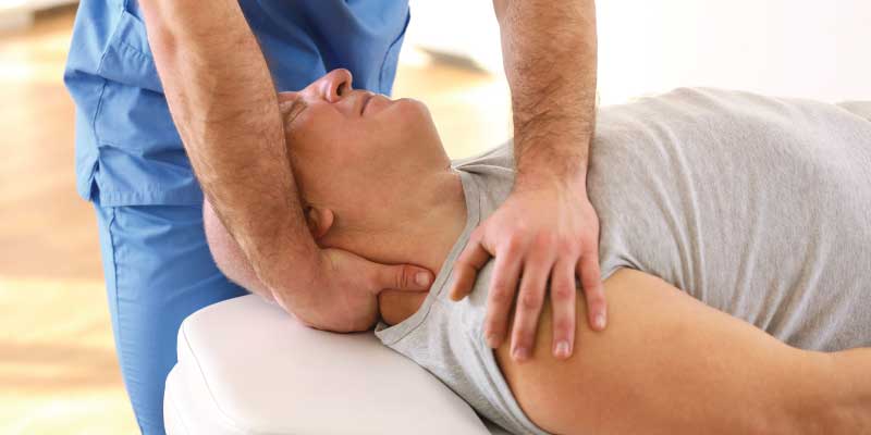 A male patient laying on a therapy table receiving a neck adjustment.