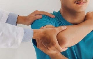 A doctor examines a male patient's right shoulder and elbow.