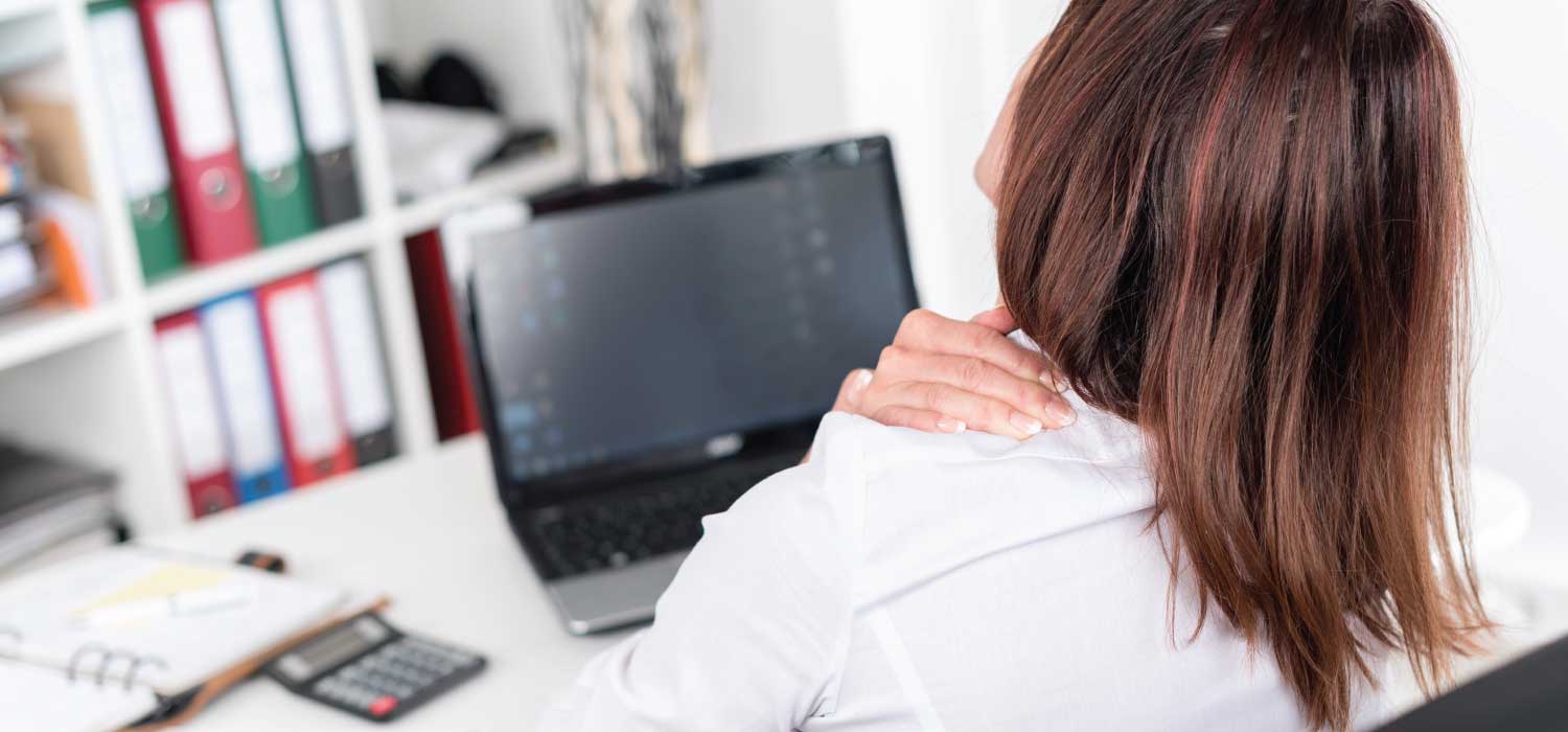 Woman working on her laptop and holding her should for neck pain.